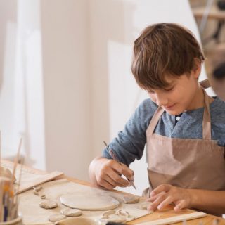 teenager boy works with clay makes  ceramic plate in pottery school.  Children arts a crafts class in workshop.